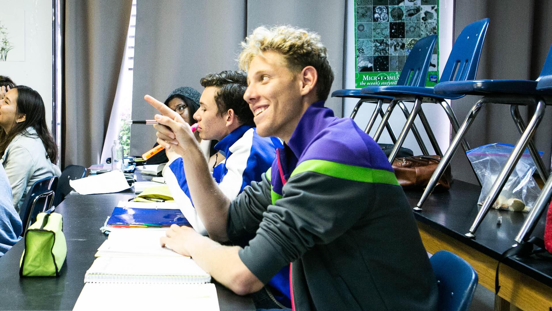 High school male student points and smiles in class.