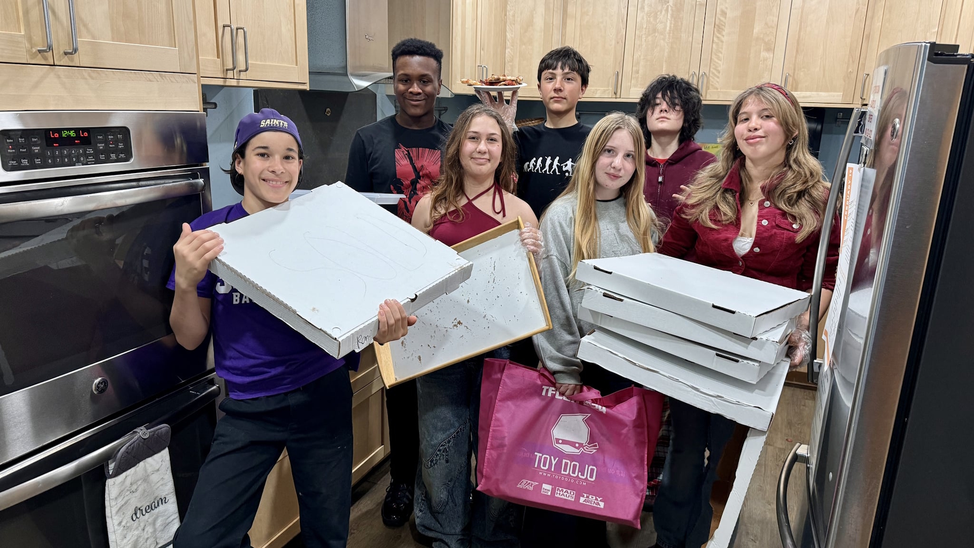 Students of all ages hold pizza boxes.